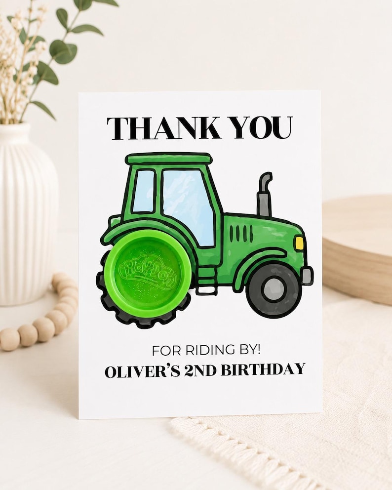 May include: A white rectangular card featuring a green tractor illustration with a bright green Play-Doh container as the rear wheel. The text reads THANK YOU, FOR RIDING BY!, and OLIVER'S 2ND BIRTHDAY in black capital letters.