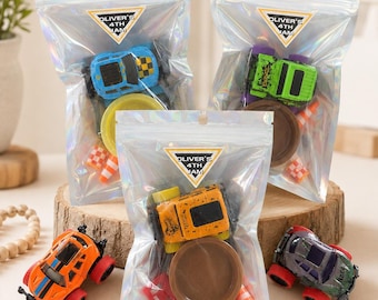 May include: Three iridescent plastic pouches containing toy race cars, small circular plastic bases, and miniature orange traffic cones. Each pouch features a triangular sticker with the text OLIVER'S 4TH JAM. Two additional toy cars sit outside.