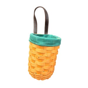 May include: A cylindrical woven basket with a light tan finish, featuring a vibrant green fabric lining at the top rim and a single dark brown leather strap attached to the side for hanging. The basket has a rounded base and a vertical structure.