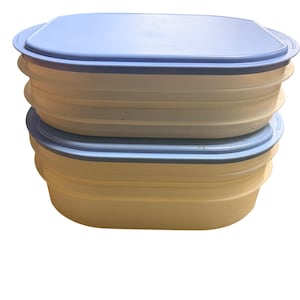 May include: Two stacked rectangular food storage containers with rounded corners. Each container features a translucent off-white base with horizontal ribbed detailing and a solid light blue plastic lid that fits securely over the top rim.