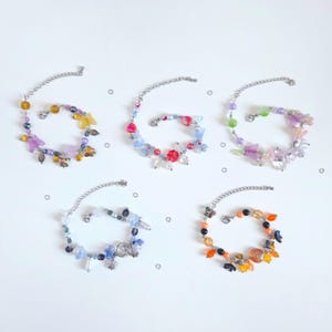 Peut inclure: Cinq bracelets composés de chaînes argentées et de perles assorties de formes et de couleurs variées, incluant des motifs de papillons, de fleurs et de cercles. Chaque bracelet est doté d'un fermoir mousqueton et d'une chaînette d'extension.
