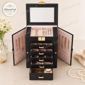 May include: A black jewellery box with a gold-tone latch and five pull-out drawers. The interior is lined with light pink fabric. The top section features a mirror, ring rolls, and earring slots. Side panels open to reveal hooks for hanging necklaces.