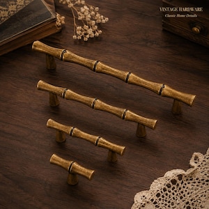 May include: Four antique brass cabinet pulls in varying lengths, each featuring a textured bamboo-inspired design with segmented nodes. The hardware displays a weathered metallic finish and includes the text VINTAGE HARDWARE Classic Home Details.