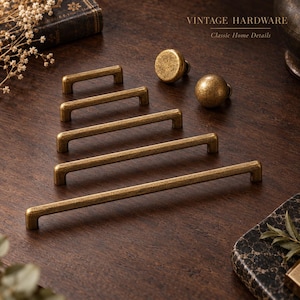 May include: A collection of five brass-toned metal cabinet pulls of varying lengths and two round cabinet knobs, all featuring a textured, aged finish. The text VINTAGE HARDWARE Classic Home Details is visible in the upper right corner of the image.