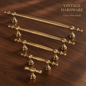 May include: Five antique brass cabinet pulls of varying lengths arranged in a descending row. Each pull features a central cylindrical bar with rounded ends and two mounting posts. The text VINTAGE HARDWARE Classic Home Details is visible.