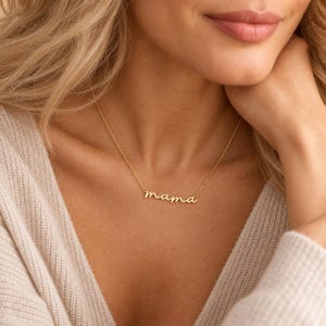 Può includere: Una collana color oro con un delicato ciondolo in corsivo che forma la parola mama. Il ciondolo è fissato a una sottile catenina color oro abbinata che poggia sulla clavicola, mettendo in risalto un design in metallo semplice e raffinato.