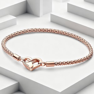 Puede incluir: Una pulsera de tono oro rosa con una cadena texturizada de cuentas y un cierre en forma de corazón. El cierre tiene grabado el nombre PANDORA. La pulsera presenta un acabado pulido y una estructura de eslabones redondeados y flexibles.