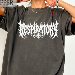 May include: A charcoal grey short-sleeve t-shirt featuring a white graphic print on the chest. The design displays the word RESPIRATORY in a stylised, jagged metal-inspired font, with a small icon of a respirator mask centred below the text.