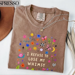 Brown t-shirt with colorful whimsical graphics and text "I REFUSE TO LOSE MY WHIMSY".