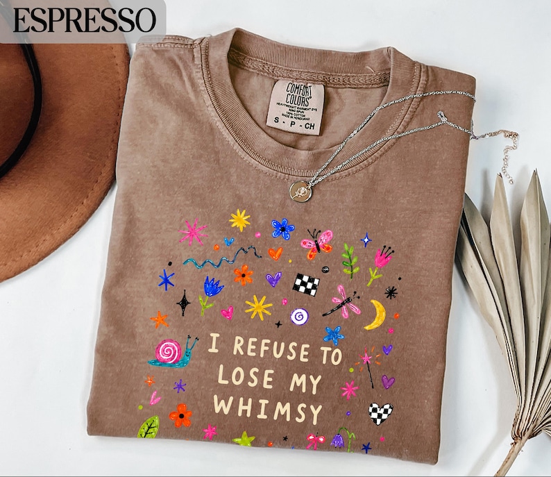 Brown t-shirt with colorful whimsical graphics and text "I REFUSE TO LOSE MY WHIMSY".