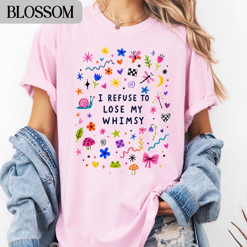 Pink t-shirt with colorful whimsical drawings and text "I REFUSE TO LOSE MY WHIMSY".