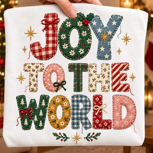 May include: A white fabric item featuring the embroidered text JOY TO THE WORLD. The letters are filled with various patterns including red gingham, green floral, blue star, and plaid prints, accented with small stitched bows and gold stars.