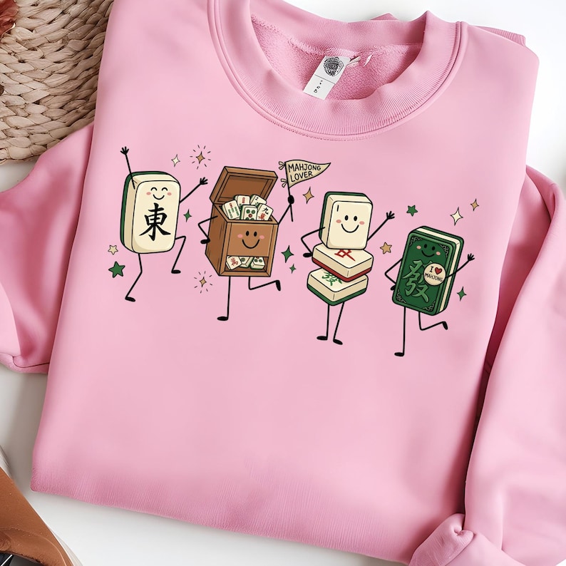Pink sweatshirt featuring a cartoon of dancing mahjong tiles and a mahjong box.