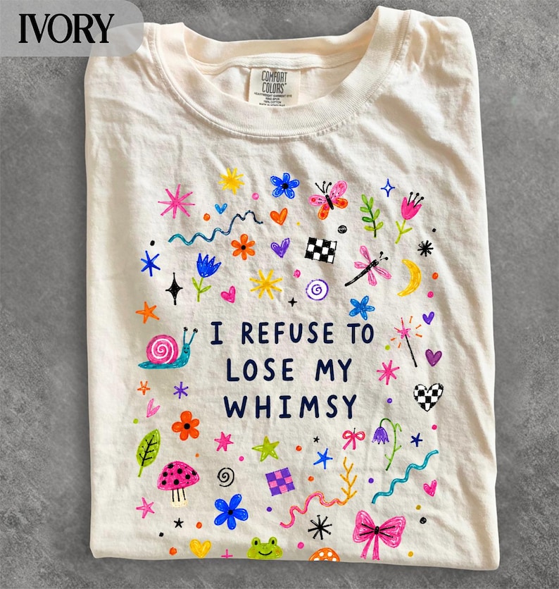 Ivory t-shirt with "I refuse to lose my whimsy" text and colorful doodle illustrations.