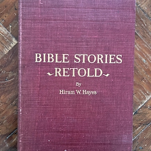 Pode incluir: Um livro bordô com letras douradas na capa. O título é "Bible Stories Retold" de Hiram W. Hayes.