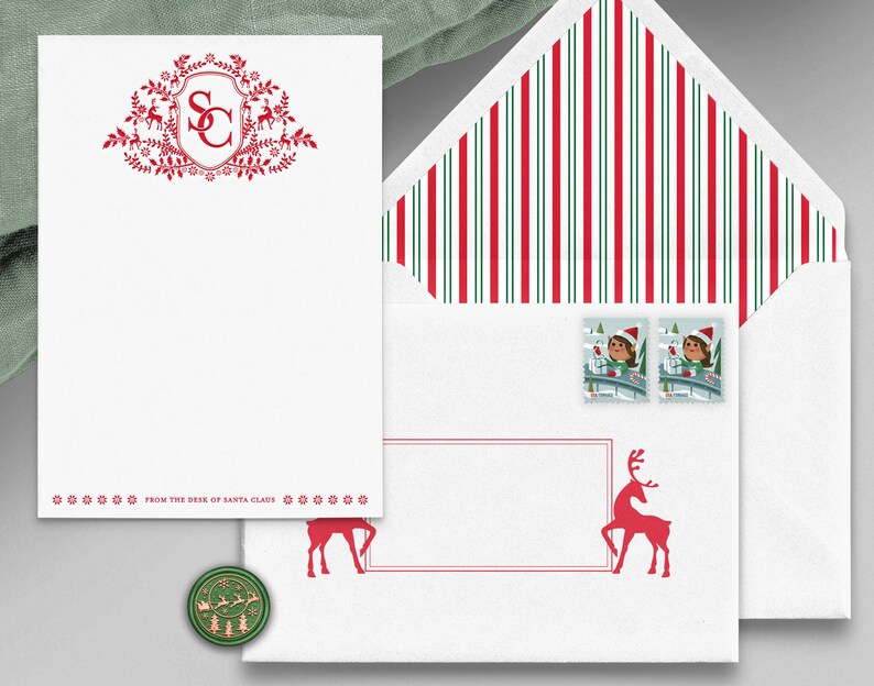 Op de afbeelding: Rode en groene kerststationery set met een rood monogram "SC" in een wapenschild met rendieren en bloemmotieven. De envelop heeft rode en groene strepen en twee postzegels met een meisje in een rode muts en een sneeuwpop. De stationery heeft de tekst "From the desk of Santa Claus".