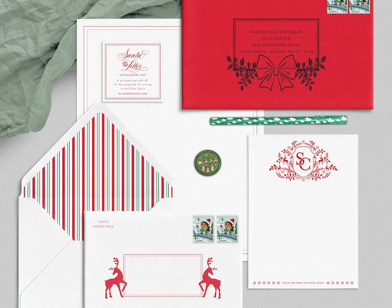 Op de afbeelding: Een witte envelop met rode en groene strepen, een witte kaart met een rood rendier en de tekst "Santa North Pole", een witte kaart met een rood monogram "SC" omringd door een krans van groen en rendieren, en een rode envelop met een zwarte stempel waarop "North Pole Postmark" en "Postmaster 8141 Postmark Drive Anchorage, Alaska 99530-9438" staat.