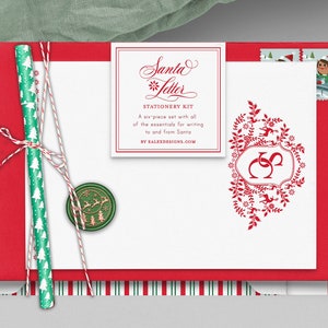 Op de afbeelding: Een rode envelop met een witte kaart erin. De kaart heeft een rood-witte gestreepte rand en een rood bloemmotief met een monogram. De kaart heeft ook een wit label met de tekst "Santa Letter Stationery Kit" en "A six piece set with all of the essentials for writing to and from Santa by FALEXDESIGNS.COM".