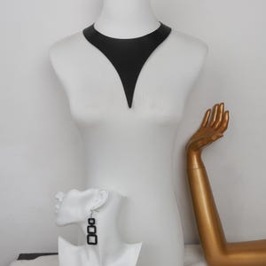 May include: A matte black V-shaped collar necklace featuring a wide, pointed design that rests against the neck. Accompanying the necklace are drop earrings, each consisting of three vertically aligned black square frames suspended from a silver hook.