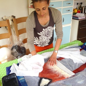 Karen hand felts the fox hat which is created by rubbing wool with soap and water. A fox hat lies on bubble wrap while Karen rubs the edges of the hat to create a neat edge around the foamy template.