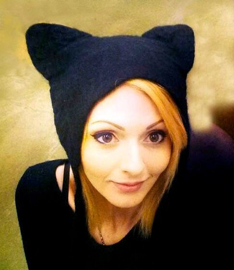 Hand felted black cat hat worn by a smiling woman with blonde hair. Black felted tassels hang down on each side. worn on stage, in film, music and theatre.