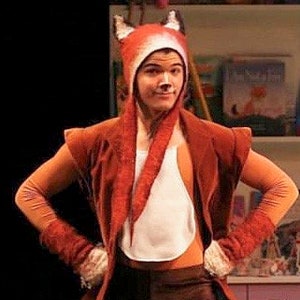 May include: A person wearing a red fox costume with a white belly and a long, white tail. The costume includes a red hat with fox ears, a red vest, and red gloves.
