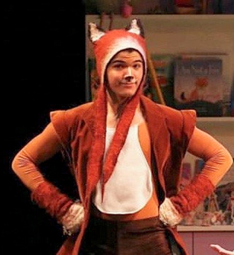 May include: A person wearing a red fox costume with a white belly and a long, white tail. The costume includes a red hat with fox ears, a red vest, and red gloves.