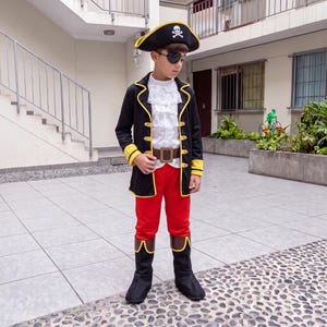 May include: A pirate costume featuring a black coat with yellow trim, a white ruffled shirt, red trousers, and a brown belt. The outfit includes a black tricorn hat with a white skull and crossbones emblem, a black eye patch, and black boot covers.