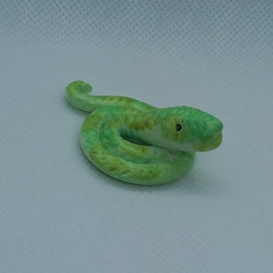 May include: A small green and white ceramic snake figurine. The snake is curled up in a coil with its head raised.