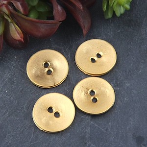 May include: Four gold-coloured metal buttons with two holes each. The buttons are round and have a slightly textured surface.