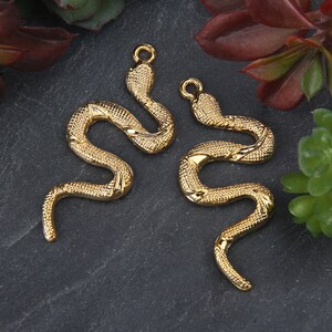 Peut inclure: Deux breloques en forme de serpent dorées à la surface texturée. Les breloques sont en forme de serpent avec son corps enroulé.