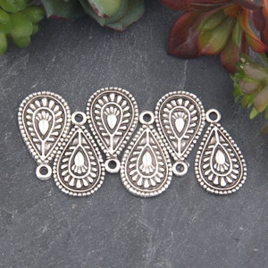 May include: Six silver teardrop-shaped metal charms with intricate paisley designs. Each charm has a small hole at the top for attaching to jewelry or other crafts.