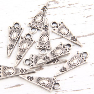 May include: A group of silver triangle charms with a decorative design. The charms have a hole at the top for attaching to jewelry or other crafts.