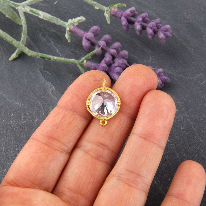May include: Gold-toned pendant with a clear round crystal. The pendant has a loop at the top for attaching to a chain.