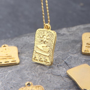 Puede incluir: Collar de oro con un colgante rectangular que presenta un diseño de sol y mano. El colgante tiene una superficie texturizada y está unido a una cadena delicada.