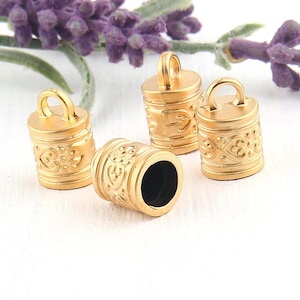 Może przedstawiać: Cztery złote metalowe końcówki sznurka z ozdobnym wzorem. Każdy koniec ma pętlę do przymocowania do sznurka lub linki.