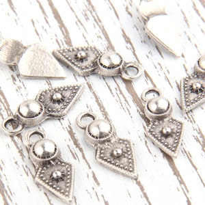 May include: Silver-toned metal pendant charms with a geometric design and a round bead. The charms have a textured surface and a loop for attaching to a necklace or bracelet.