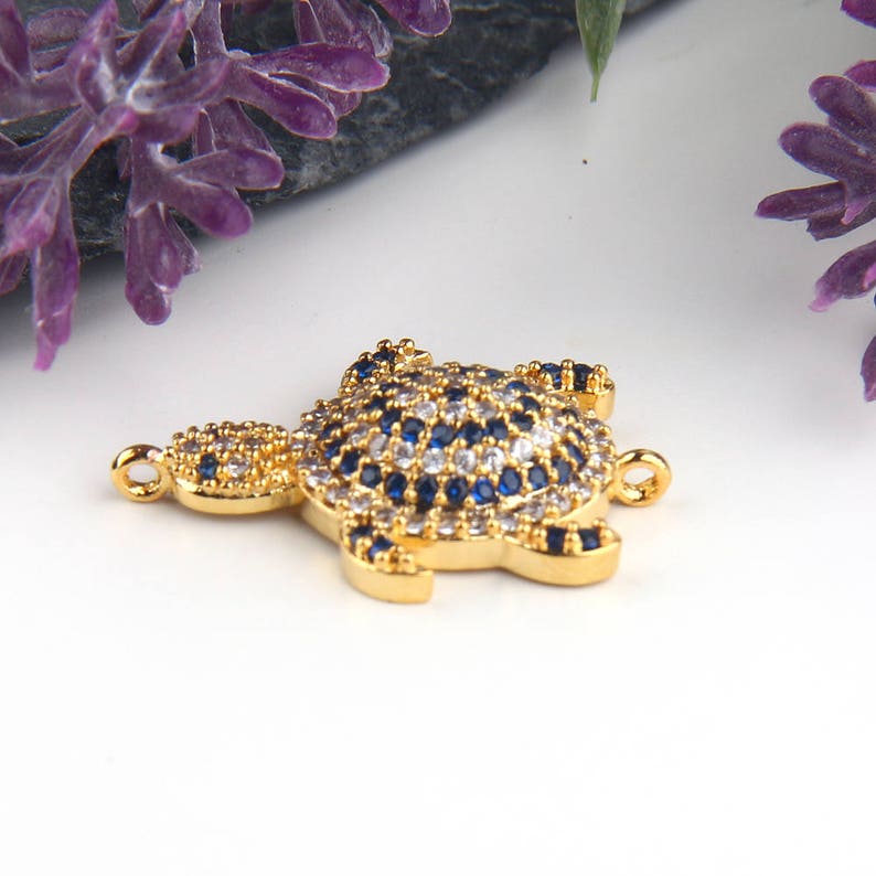 May include: Gold-tone turtle charm with blue and white crystal accents. The charm has two jump rings for attaching to jewelry.
