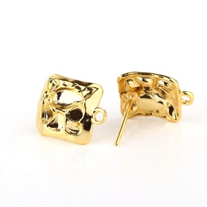 May include: A pair of gold-tone earring findings with a square shape and a textured design. The findings have a post and a loop for attaching earrings.
