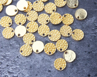 May include: A collection of gold-colored metal round charms with a textured surface. The charms are scattered on a gray background.