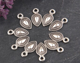 May include: A collection of silver-toned teardrop-shaped charms. Each charm features a detailed design with a central teardrop shape, surrounded by a dotted border. The charms have a loop at the top for attaching to jewelry.