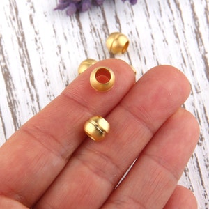 May include: Gold-toned metal beads with a smooth, rounded surface. The beads have a slightly raised center band.