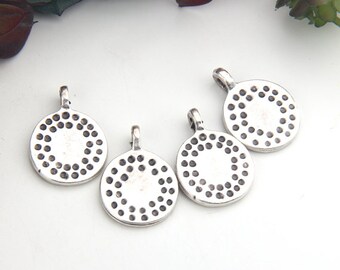 Peut inclure: Quatre pendentifs ronds argentés avec une petite boucle en haut. Chaque pendentif présente un motif de petits points foncés sur le bord, créant un design circulaire. Les pendentifs sont sur une surface blanche.