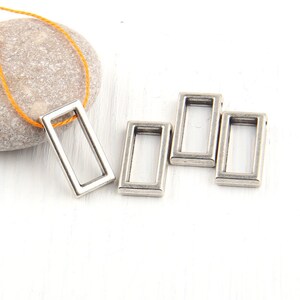 May include: Four silver-toned metal rectangular jump rings. The rings are open and have a smooth finish.