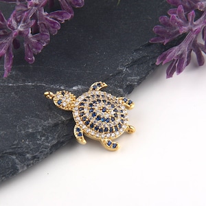 May include: A gold-tone turtle charm with blue and white crystal accents. The charm is perfect for adding a touch of whimsy to jewelry projects.