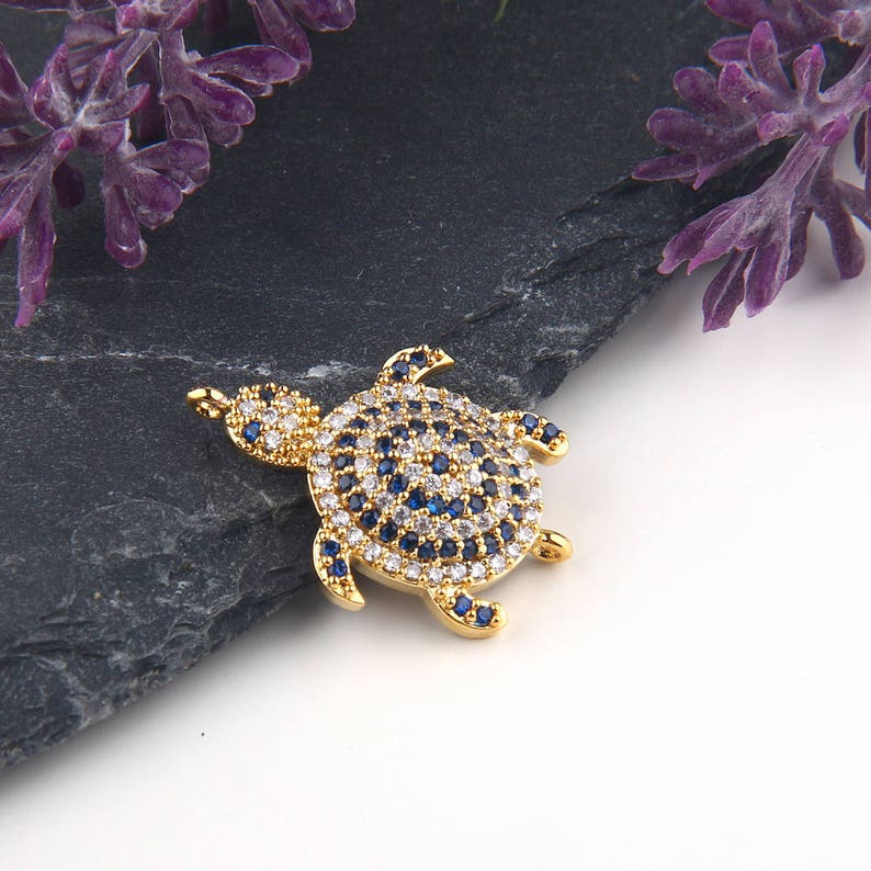 May include: A gold-tone turtle charm with blue and white crystal accents. The charm is perfect for adding a touch of whimsy to jewelry projects.