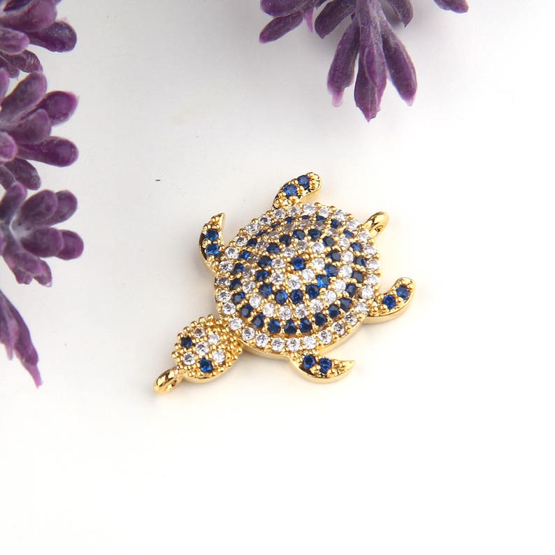 May include: Gold-tone turtle charm with blue and white crystal embellishments. The charm has a loop for attaching to a necklace or bracelet.