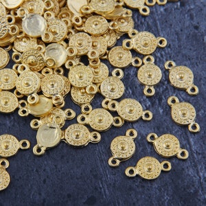 May include: A pile of gold-coloured metal connector charms with a circular design and two loops. The charms are scattered on a dark grey surface.