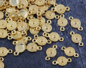 May include: A pile of gold-colored metal connector charms with a circular design and two loops. The charms are scattered on a dark gray surface.