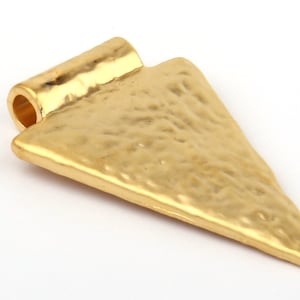 May include: Gold-toned metal arrow pendant with a textured surface. The pendant has a loop at the top for attaching to a chain or cord.